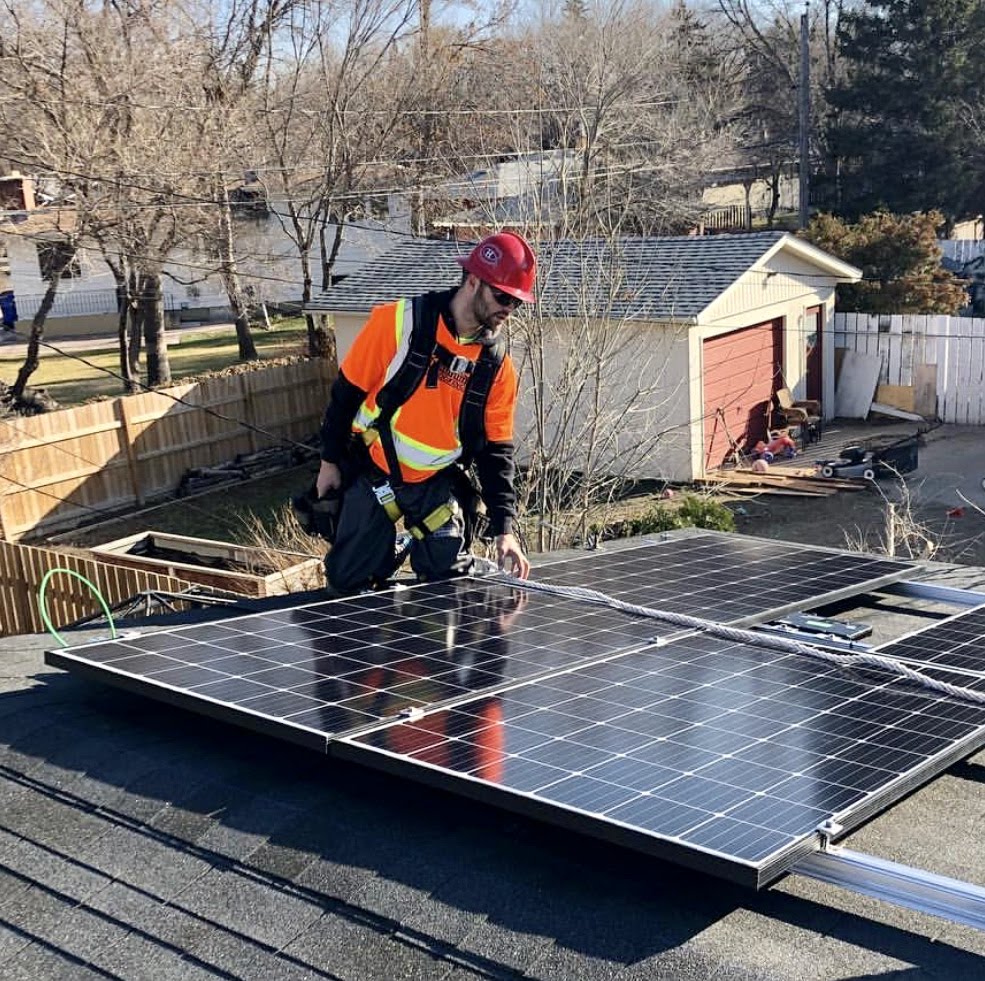 Solar technician in safety gear installing panels on residential rooftop